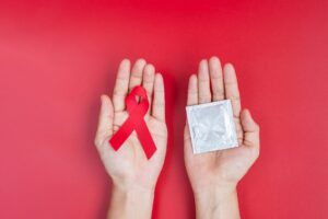 hand-holding-red-ribbon-and-condom-world-aids-day-2023-11-27-05-35-50-utc-2048x1365