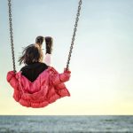 Little girl on the swing watching the sunset over the sea