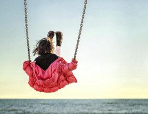 Little girl on the swing watching the sunset over the sea